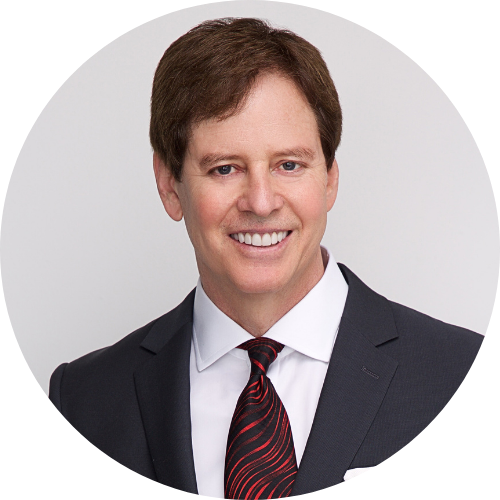 Business professional in dark suit and red tie, smiling in a corporate headshot taken in Dallas. | For Companies |