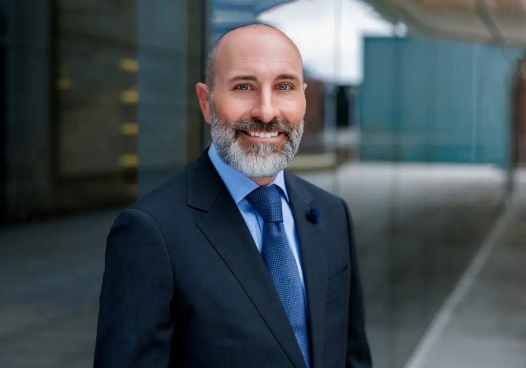 Portrait of a Smiling Man in a Navy Suit and Blue Tie Outdoors with a Glass Building in the Background