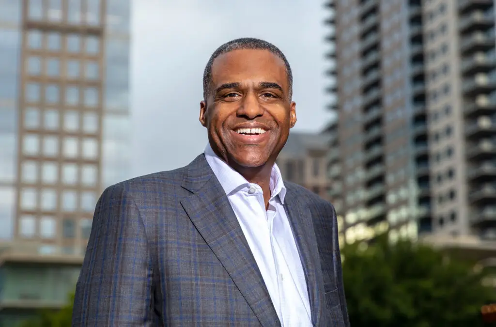 Smiling Man in a Blue Plaid Suit Outdoors in an Urban Setting with Tall Buildings in the Background