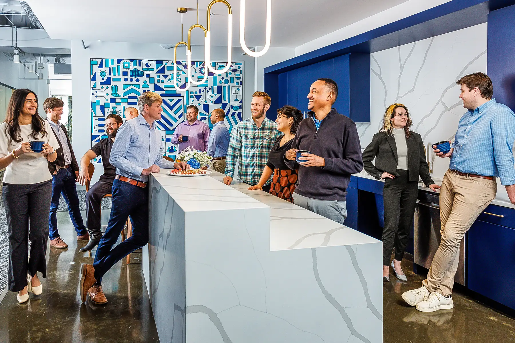 Group of Colleagues Chatting and Enjoying Snacks in a Modern Office Break Area with a Marble Island Centerpiece Blue Accents and Ambient Lighting
