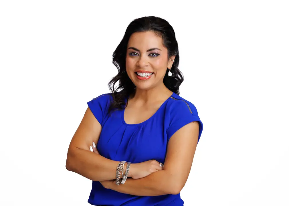 Smiling Woman with Dark Hair in a Blue Blouse Arms Crossed Against a White Background