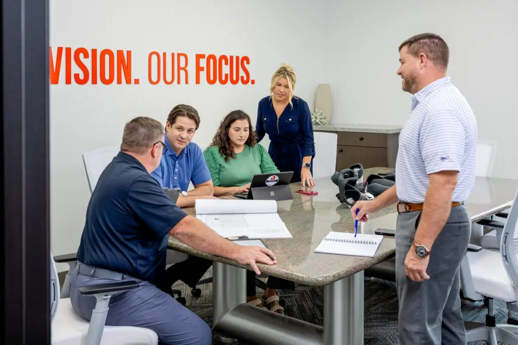 Team of Five Collaborating at a Conference Table with Documents and Tablets Bold Red Vision Our Focus on the Wall Behind Them
